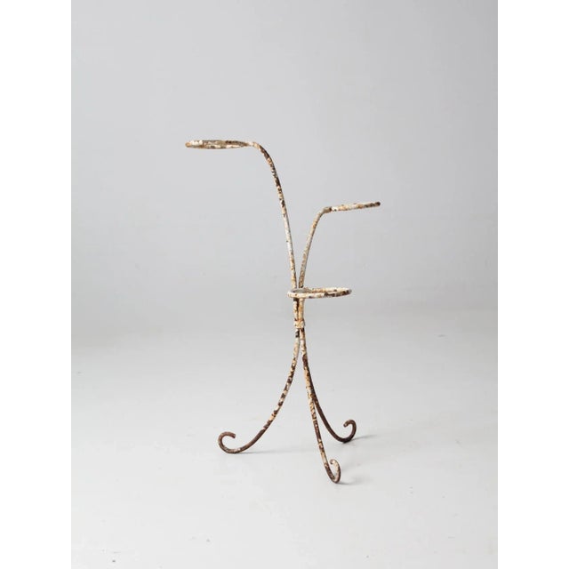 Vintage white iron ring plant stand with a slender, curving form. The openwork structure features three circular rings...