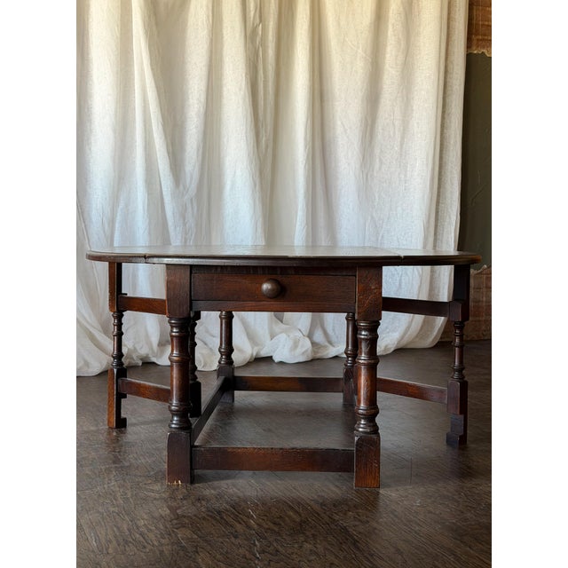 This charming vintage drop-leaf coffee table features a rich, dark wood finish and a classic oval top with hinged gate-leg...