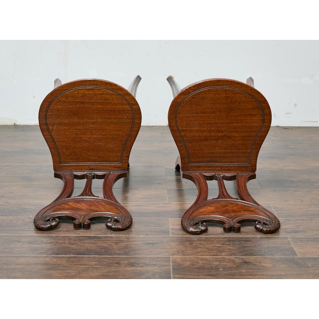 This pair of English mahogany hall chairs dates to the 19th century and stands out for its dramatic carved backrests...
