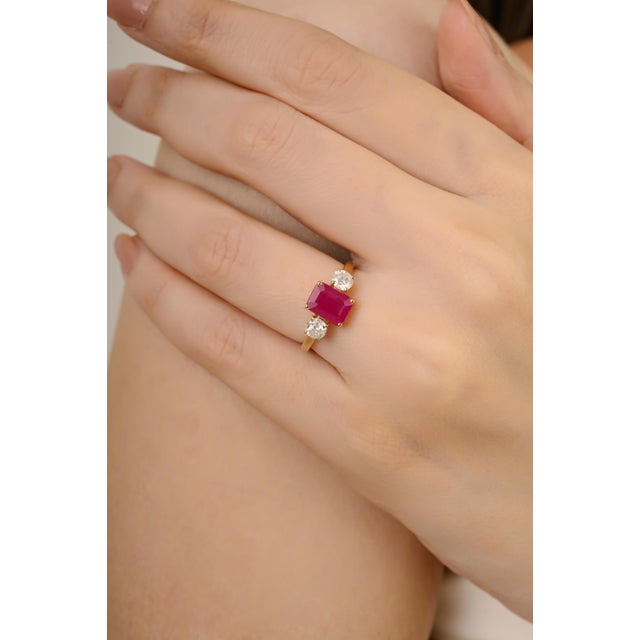 This ring is crafted in 14K yellow gold and features a 1.48 carat emerald cut ruby at the center, flanked by two round...