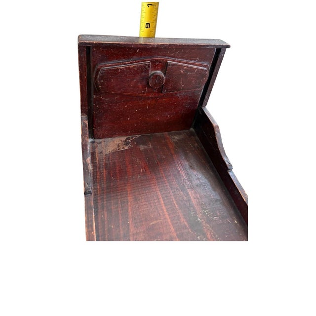A charming late 19th-century wooden doll bed featuring hand-carved details and a rich, dark finish worn beautifully with...