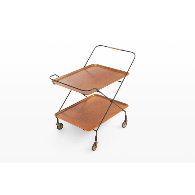 A charming vintage serving trolley designed by paul nagel for jie gantofta, combining warm wooden trays with a slender...
