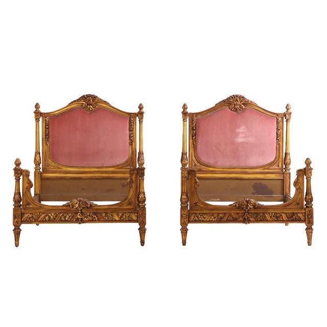 A graceful pair of French twin beds each with a finely carved giltwood frame with classical detailing, including central...