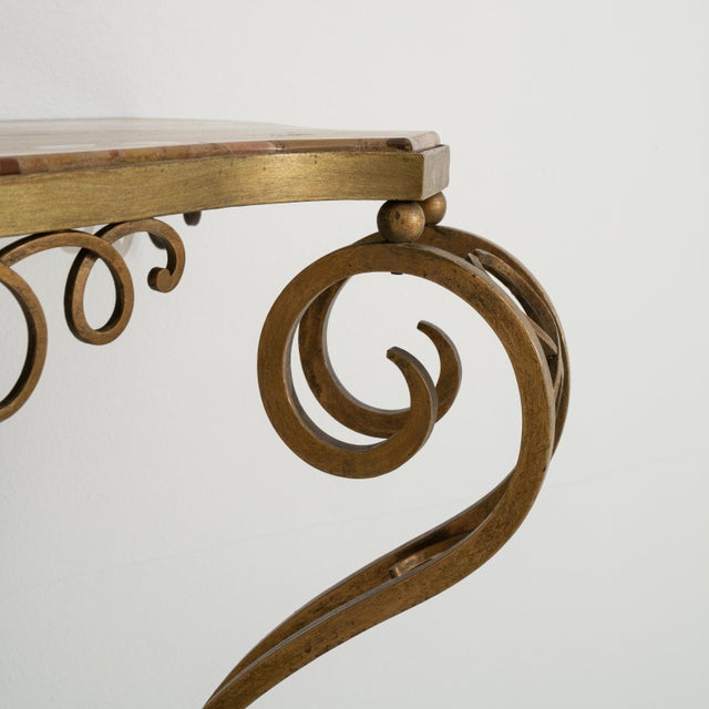 An Art Deco console table featuring an ornate wrought iron base. The top is finished with marble, offering a contrast...