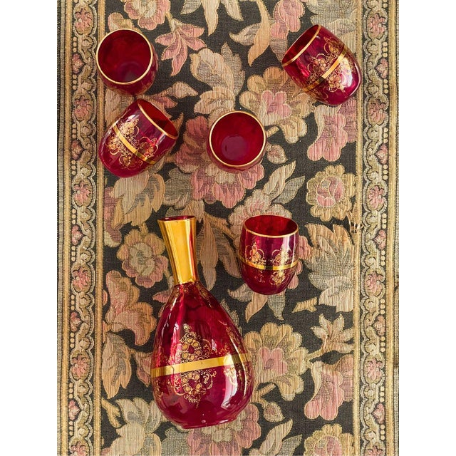Vintage Italian-style glassware set featuring a rich ruby-red glass with elaborate gold filigree and floral decoration....