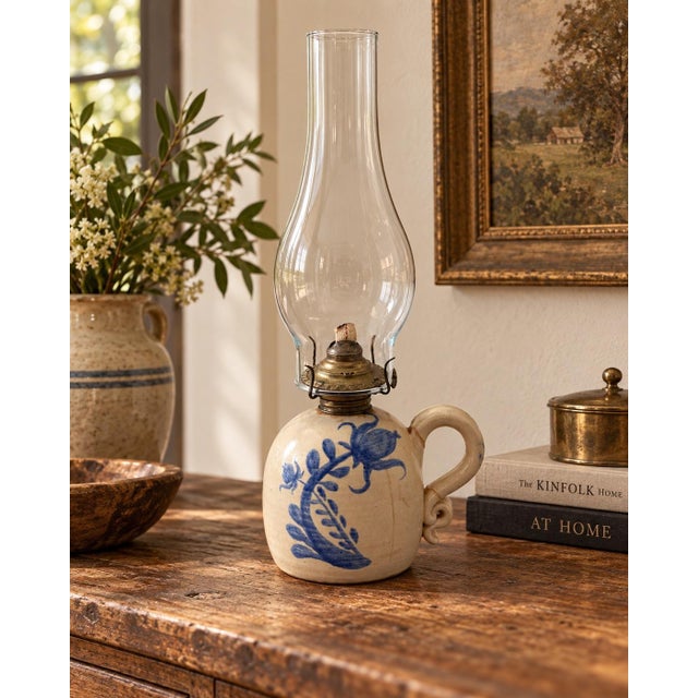 Charming antique stoneware oil lamp featuring a rounded cream ceramic body with hand-painted cobalt blue floral decoration...