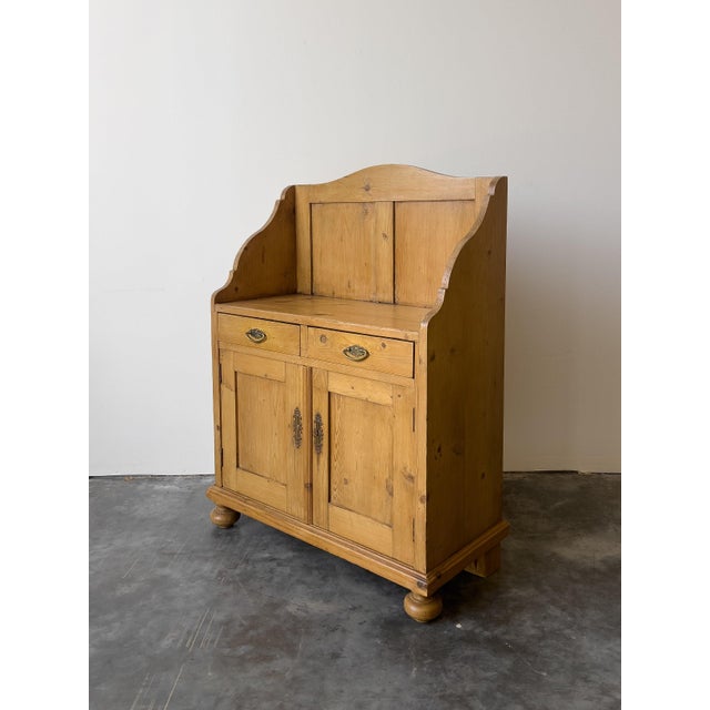 A charming antique Dutch pine cupboard with a paneled gallery back. Two drawers with brass pulls above two paneled cabinet...