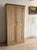A tall English larder cupboard in pale pine, twin paneled doors with a small turned center knob and a stepped cornice...