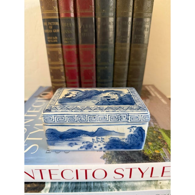A charming vintage blue and white porcelain trinket box featuring hand-painted landscape scenes on all sides and the lid....