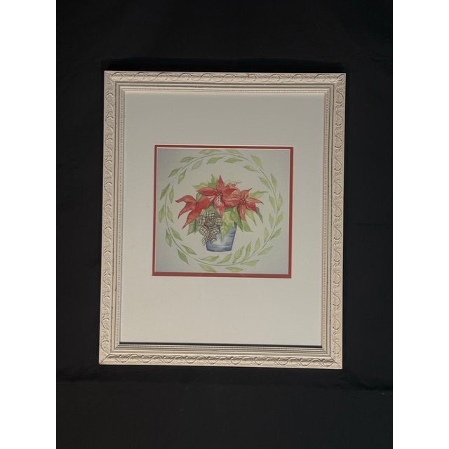 Decorative framed floral wall art featuring red poinsettia-style flowers in a blue pot with a soft green leaf wreath...