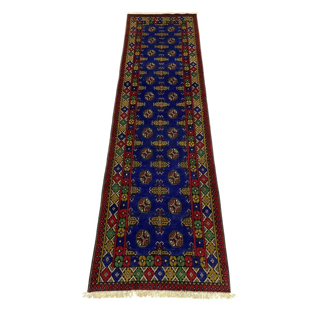 This tribal Oriental wool runner features two columns of repeating Mori Gul medallions across a vivid cobalt-blue field....