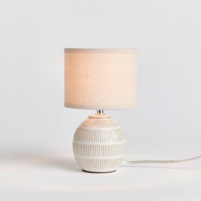 With a petite ceramic body and a soothing taupe glaze, this lamp adds warmth to any setting. Topped off with a natural...