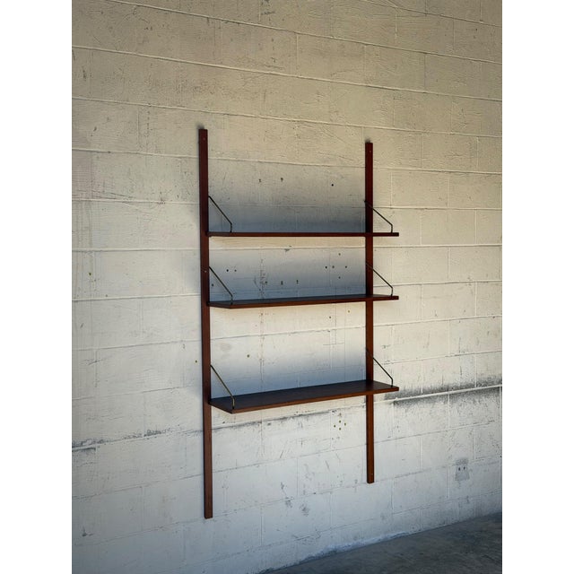 Vintage Danish Modern wall-mounted teak shelving system by Cado, featuring three adjustable wooden shelves supported by...