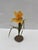 This artwork presents a delicate flower crafted from paper, wire, and paint, emerging from a textured cement base. The...