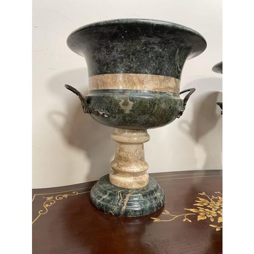 A striking pair of heavy, neoclassical marble urns with elegant brass side handles. Beautifully shaped with contrasting...