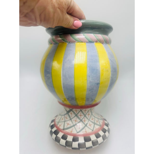 This is a colorful, hand-painted ceramic urn-style vase with a rounded body and pedestal base. It features bold vertical...