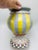 This is a colorful, hand-painted ceramic urn-style vase with a rounded body and pedestal base. It features bold vertical...