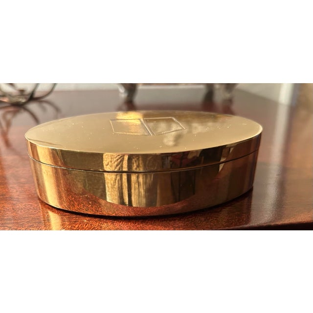 Oval brass box with lid and velvet interior. Very heavy weighs 1lb, 4 ounces. The lid features geometric logo composed of...