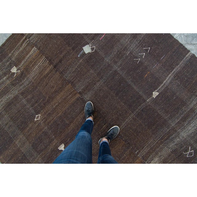 A beautiful monotone vintage kilim featuring abstract designs in beige, red, and orange on dominant hues of brown. This...