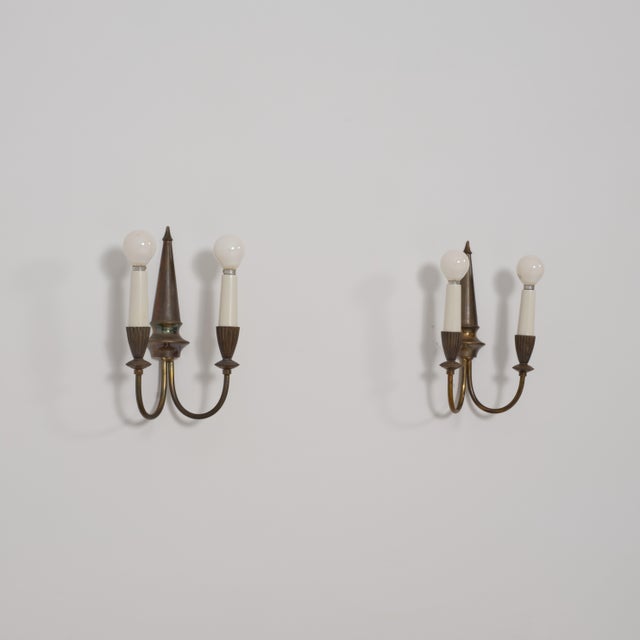 A distinctive and subtly playful pair of italian wall sconces from the 1950s, defined by a sculptural composition in brass...