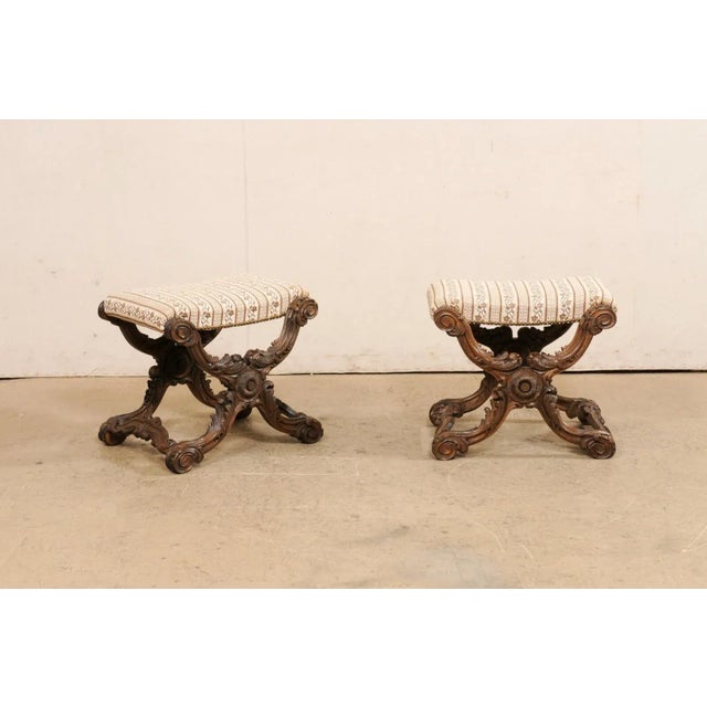 A pair of French ornately carved wood and upholstered stools from the 19th century. These antique stools from France each...