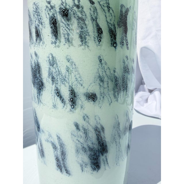 This work of glass art is a light teal layered glass with drawings of people silhouetted in navy blue made using the Graal...