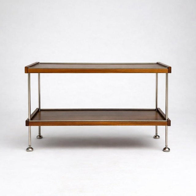 A sleek vintage drinks cart crafted in warm teak and polished chrome, exemplifying elegant mid-century modern design. The...