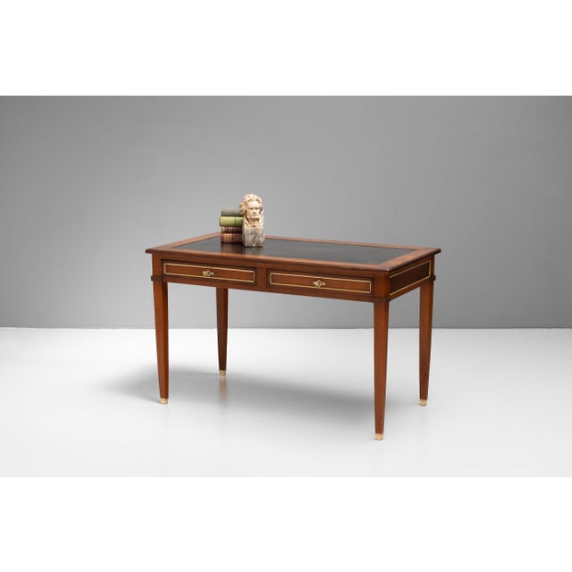Two drawer French writing table in walnut with aged inset black leather top. Circa 1920.