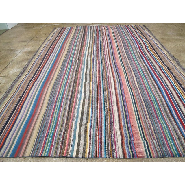 This mid-20th century Turkish flatweave Kilim rug, features a vibrant and eclectic striped design that embodies the rich...