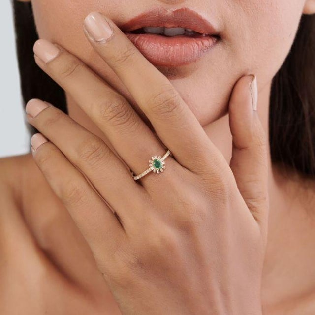 This elegant sunburst ring features a vibrant 0.08 ct emerald and diamond, set in 14k yellow gold. The center stone...