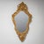 Wall mirror in elongated shield form with a giltwood frame. The frame is richly carved with C-scrolls, shell motifs, and...