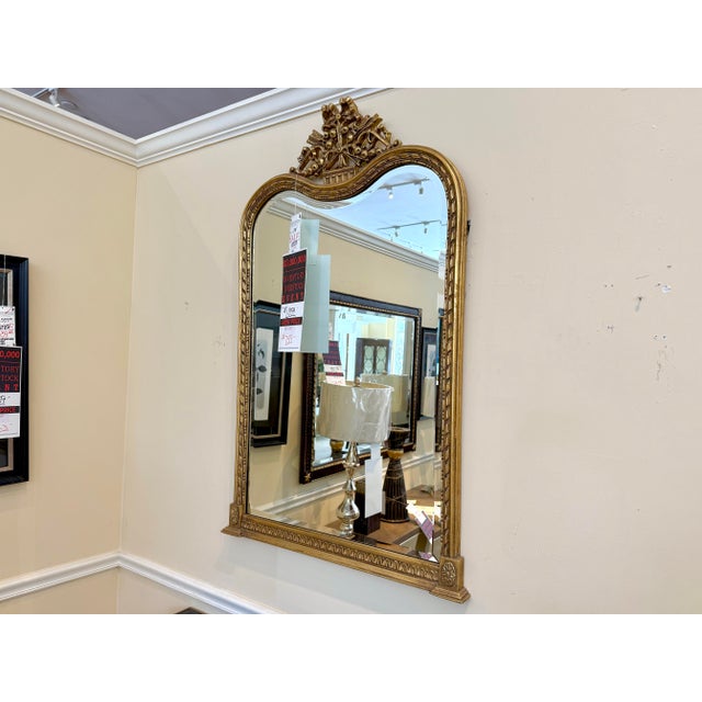 An elegant wall mirror featuring a gracefully shaped frame with a serpentine top, carved crest, and warm gilt finish. The...