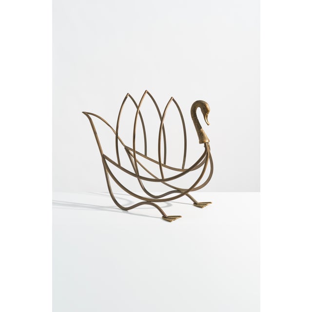 A large, elegant vintage brass magazine rack in the form of a stylized swan, attributed to Maison Jansen. The looping...