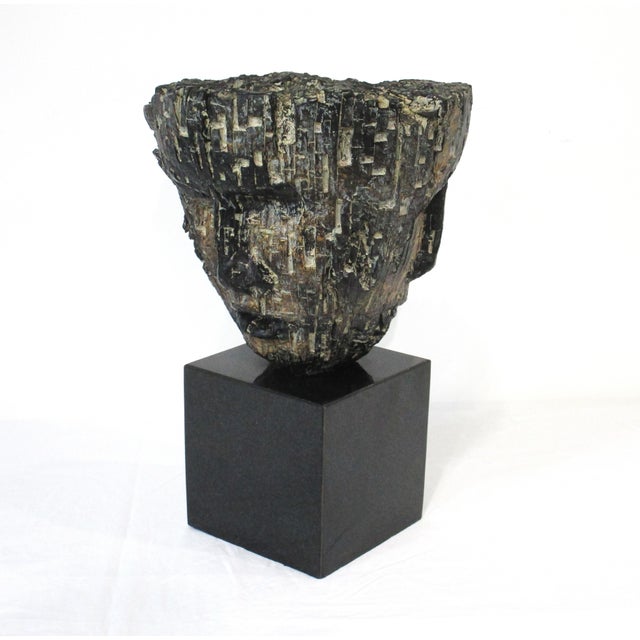 A Brutalist head sculpture with three faces at different angles sitting on a dark charcoal marble slab square base. The...