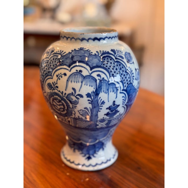 A finely decorated Delft jar featuring intricate hand-painted blue-and-white floral and landscape motifs. The graceful,...