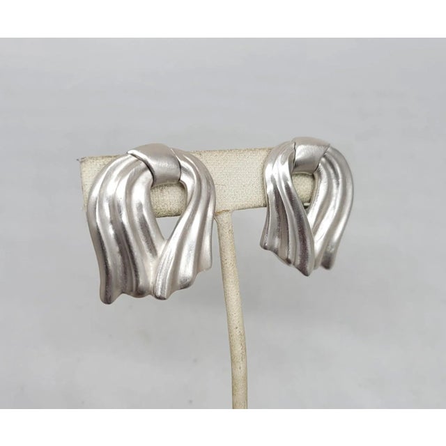 This is part of Chairish’s Costume Jewelry assortment. 1980s Modernist rhodium plated wavy ribbon clip earrings. Marked...