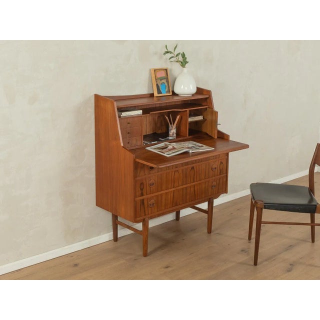 A classic bureau from the 1960s. Its walnut veneer body features a pull-out work surface, three small and three large...