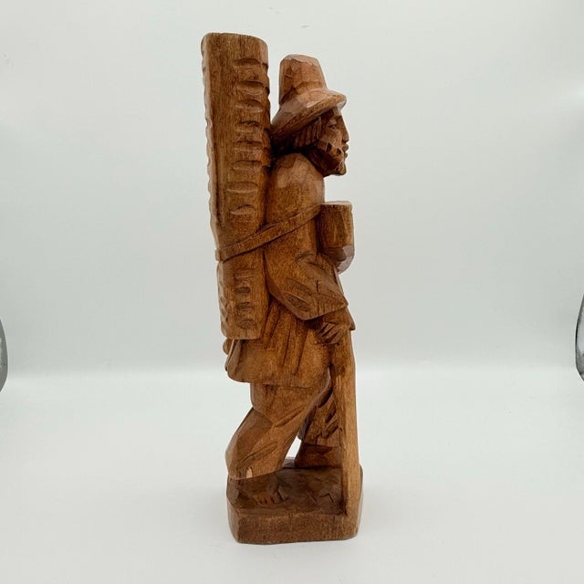 A wonderfully sculptural vintage hand-carved wood figure depicting a traveling peddler or village merchant carrying his...