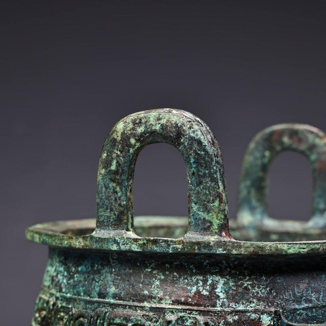 Impressive archaic-style bronze tripod ding vessel. Raised twin upright handles sit atop the wide rim. The rounded body is...