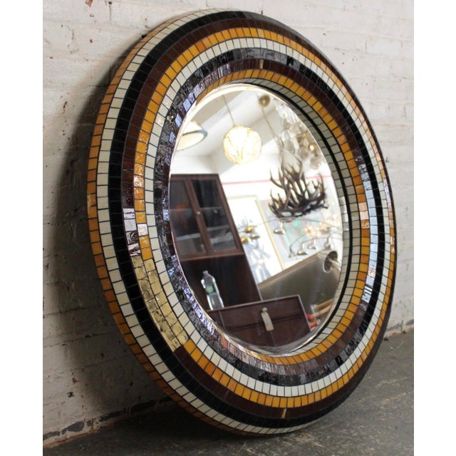 A striking round mirror featuring a vibrant mosaic tile border in classic mid-century hues. The handcrafted design...