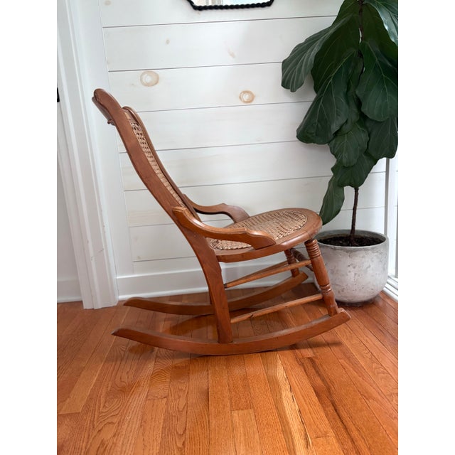 Vintage early 20th century Colonial Revival rocking chair featuring a hand-caned seat and back with a decorative burlwood...