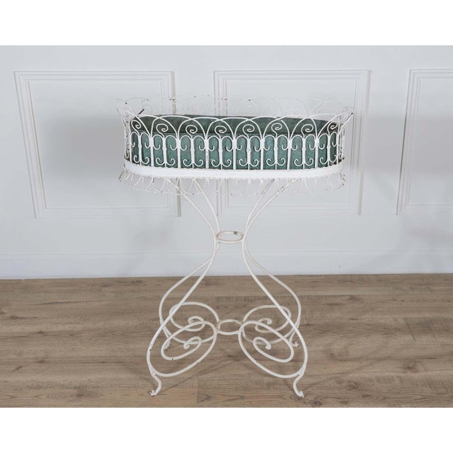 This 20th-century wrought iron planter features a rectangular basket supported by a scrollwork base. The upper section is...