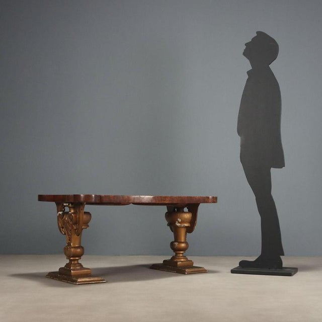 Coffee table. Shaped top veneered in walnut burl, supported by a pair of antique carved vases, originally painted and...