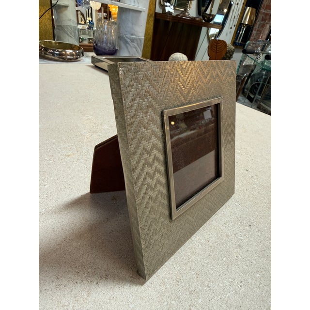 Elegant vintage picture frame featuring a richly textured silver-tone metal finish with a subtle geometric woven pattern....