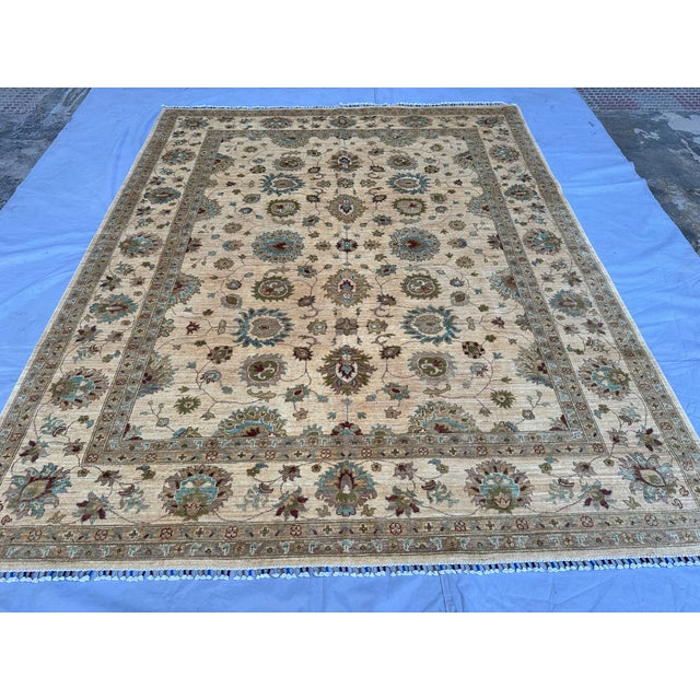This elegant hand-knotted wool area rug features a classic Oushak style. The open center field has a warm cream background...