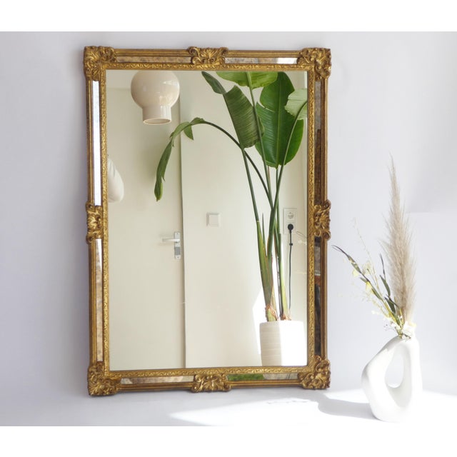 A large vintage rectangular mirror with gold gilt wood details. The mirror is made in Belgium and has a brand in the back....